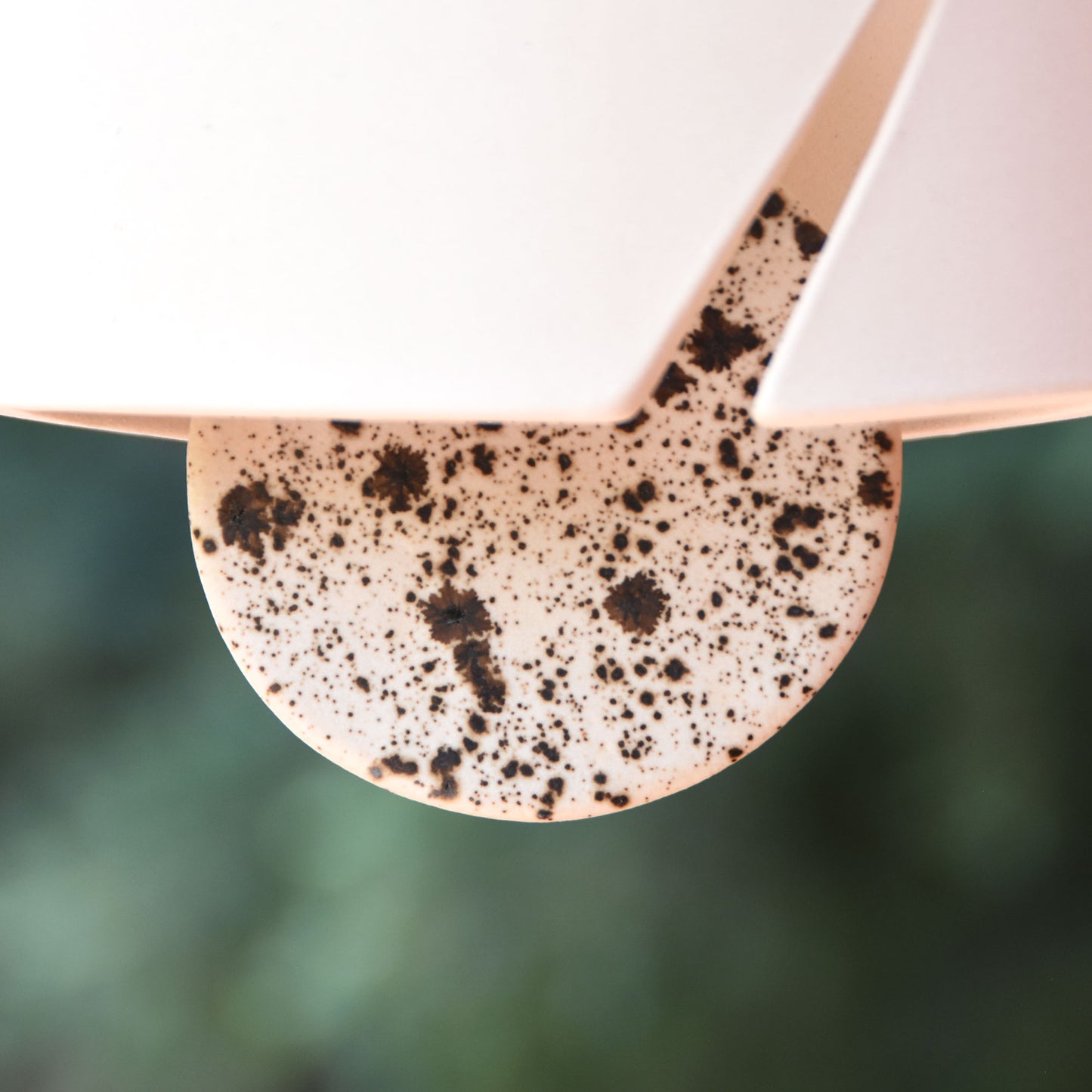 closeup of speckled black and white ceramic wind clapper hanging from modern ceramic wind chime in elegant white