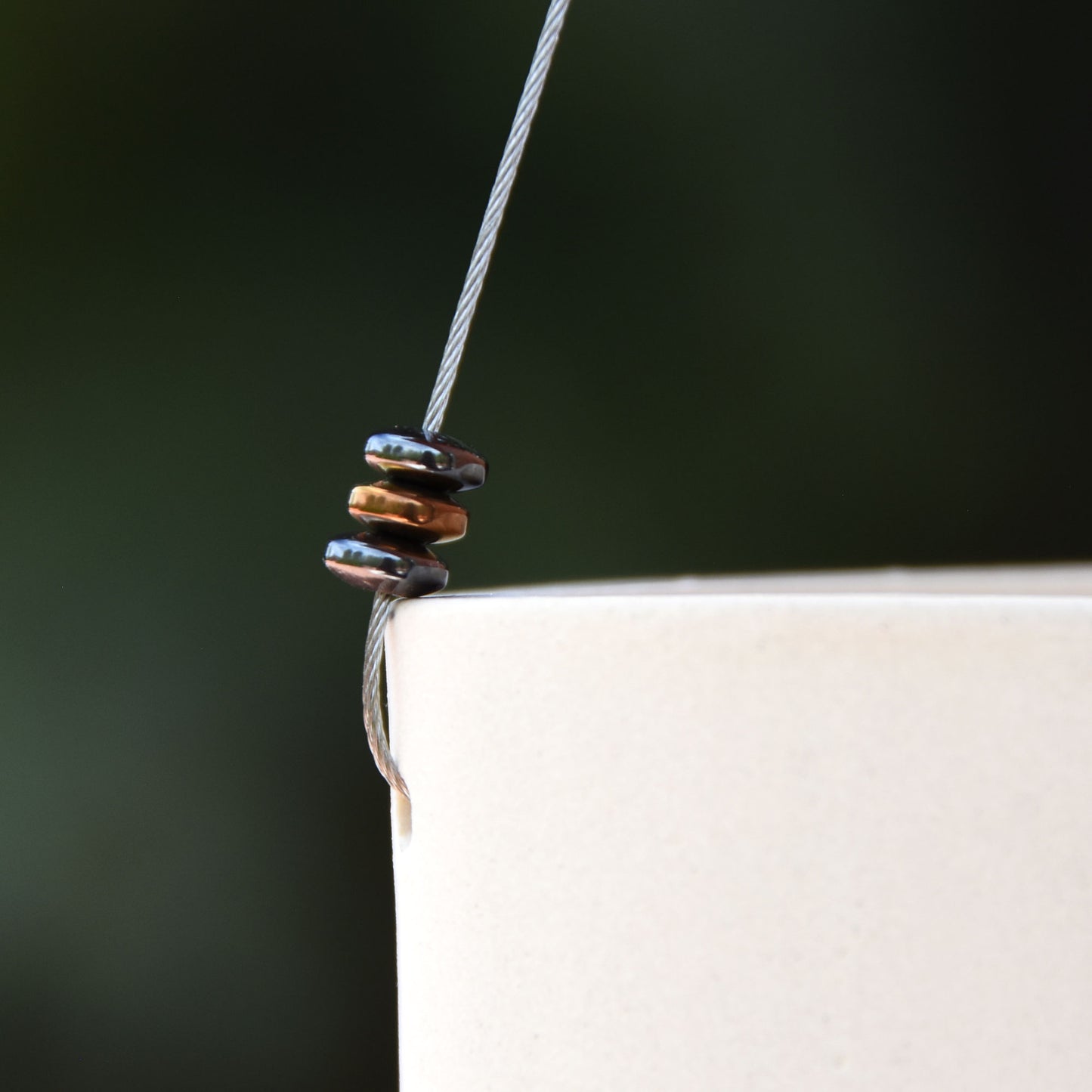 closeup of three modern metallic beads attached to steel wire which holds up ceramic white wind chime