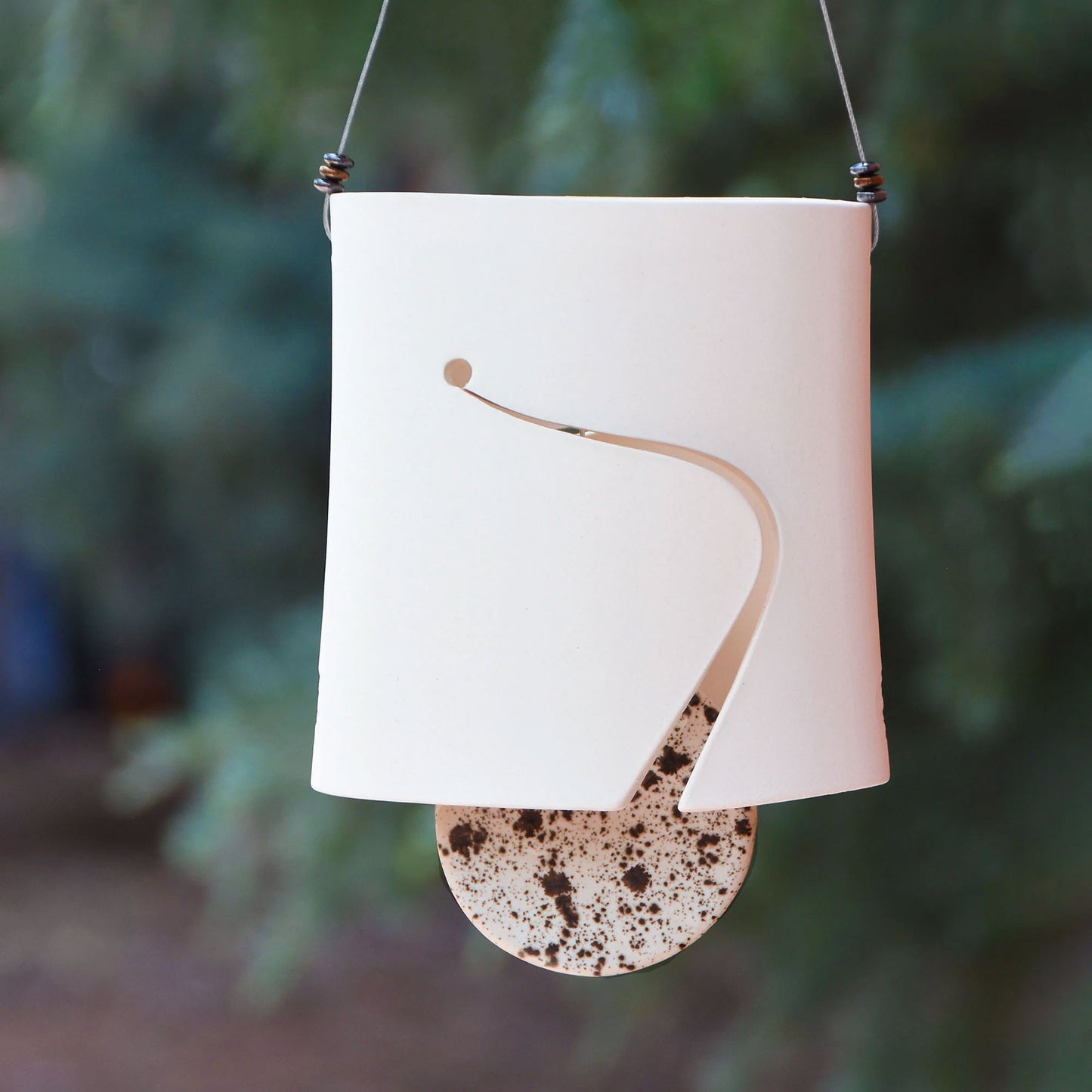 Modern white ceramic wind chime with curved cutout and speckled black and white round clapper hanging from steel wire which is adorned with three modern steel beads on each side