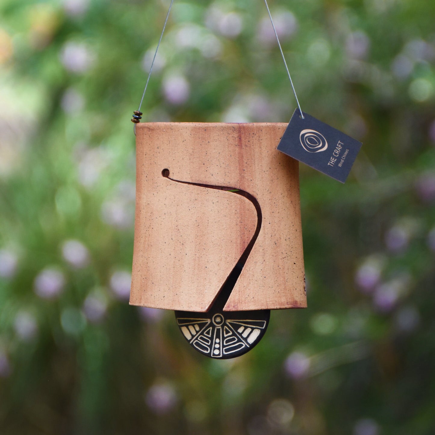 Modern, speckled buff ceramic wind chime bell that was stained with red iron oxide. The bell features a black and white sgraffito wind clapper carved with an abstract motif