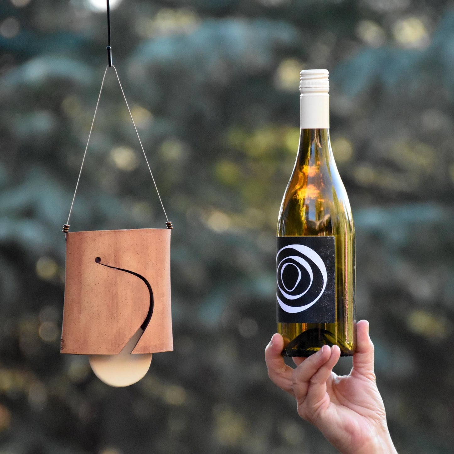 Image showing speckled buff ceramic wind chime bell with white clapper and wine bottle next to it for size comparison