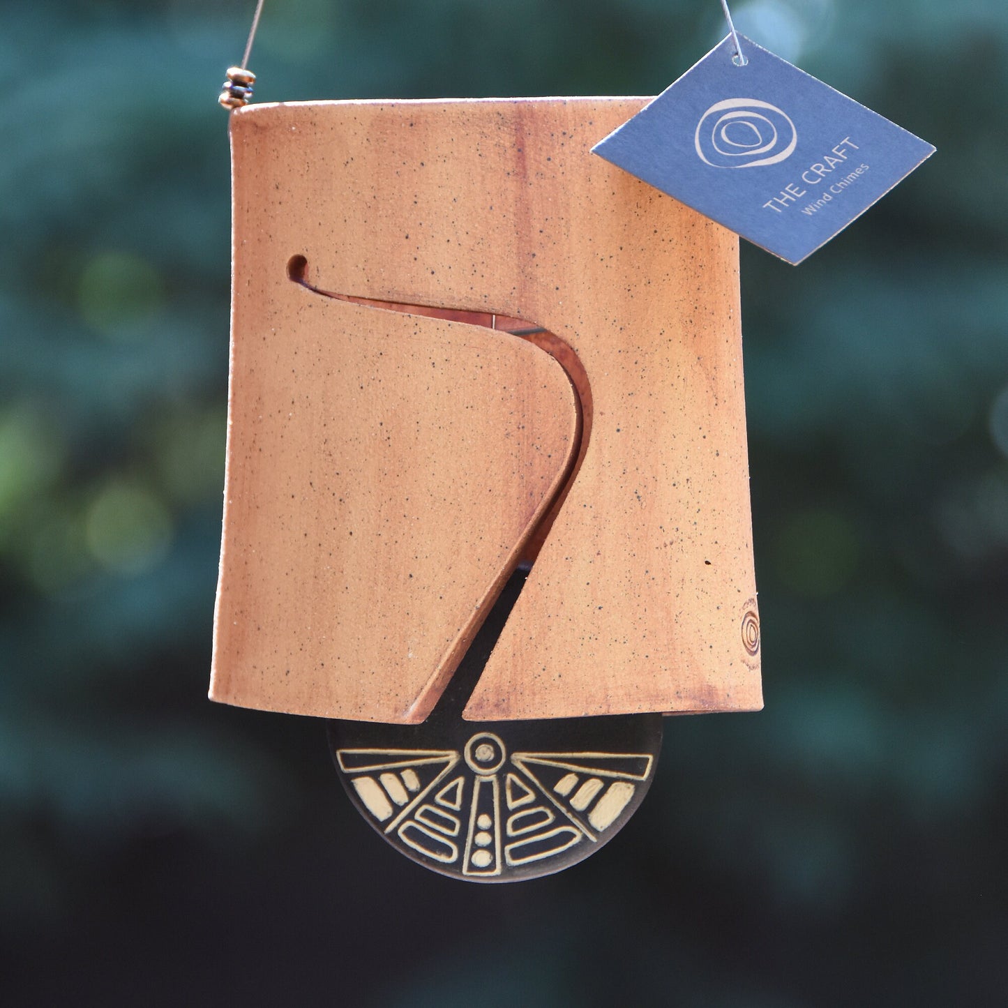 Modern, speckled buff ceramic wind chime bell that was stained with red iron oxide. The bell features a black and white sgraffito wind clapper carved with an abstract motif