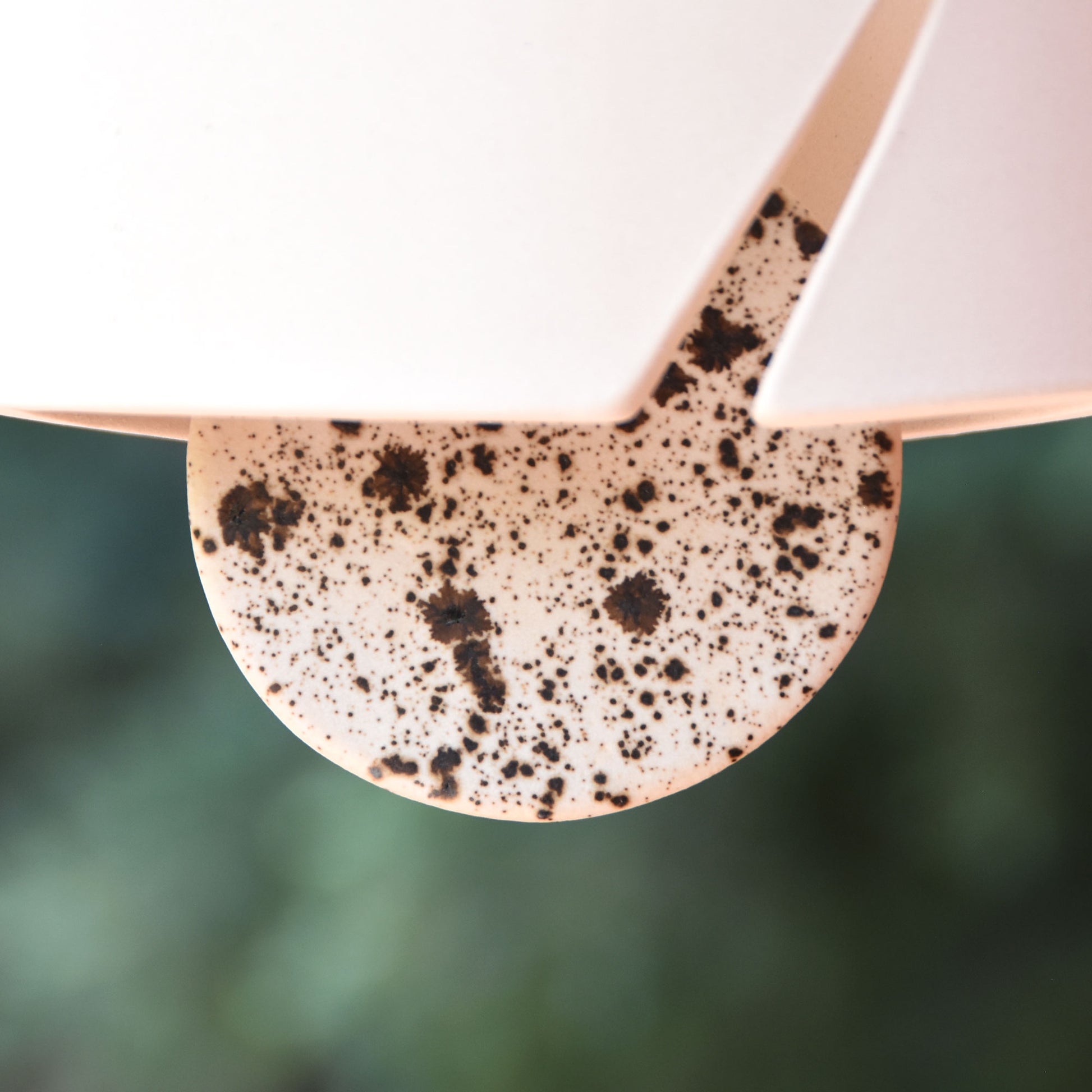 closeup of speckled black and white ceramic wind clapper hanging from modern ceramic wind chime in elegant white