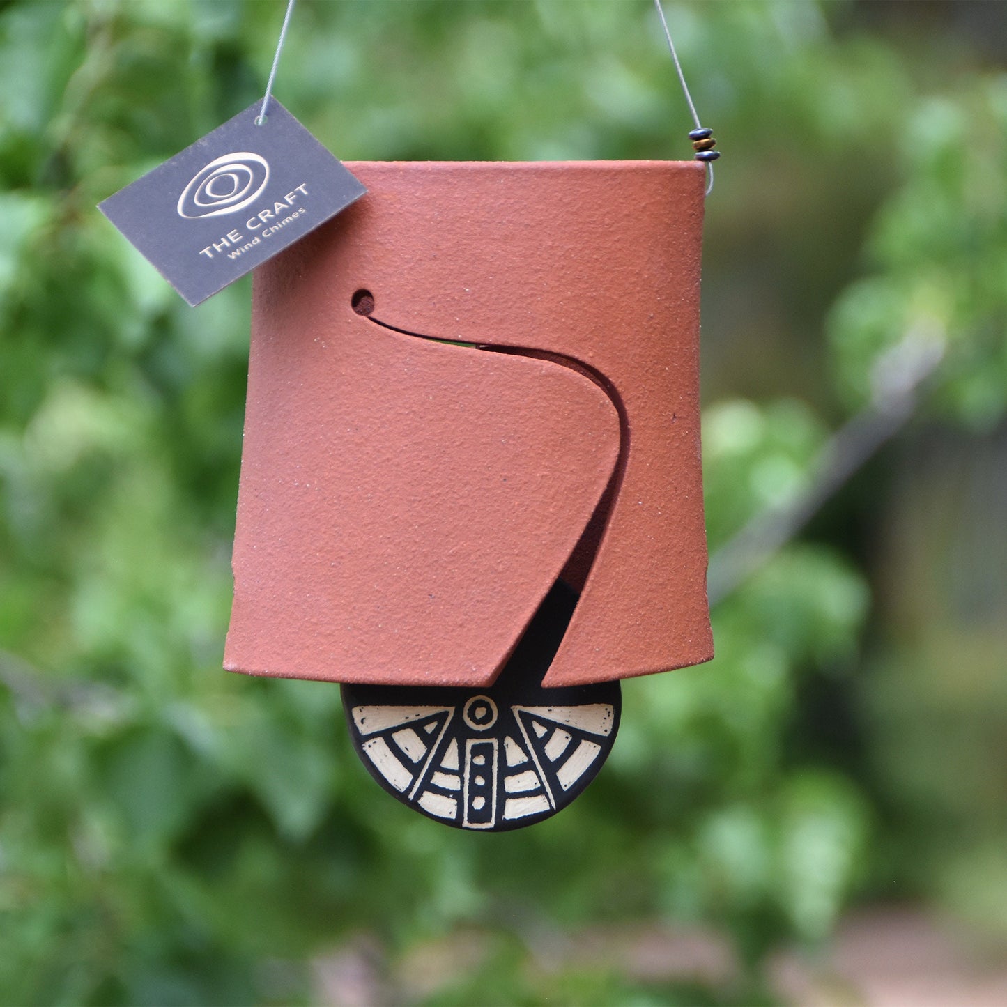 Closeup of modern, rustic red ceramic wind chime bell showcasing a black and white wind clapper carved in an abstract motif using the sgraffito technique