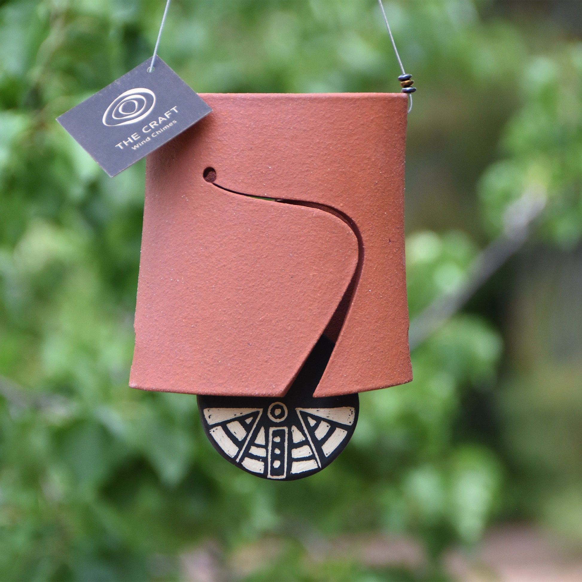 Closeup of modern, rustic red ceramic wind chime bell showcasing a black and white wind clapper carved in an abstract motif using the sgraffito technique