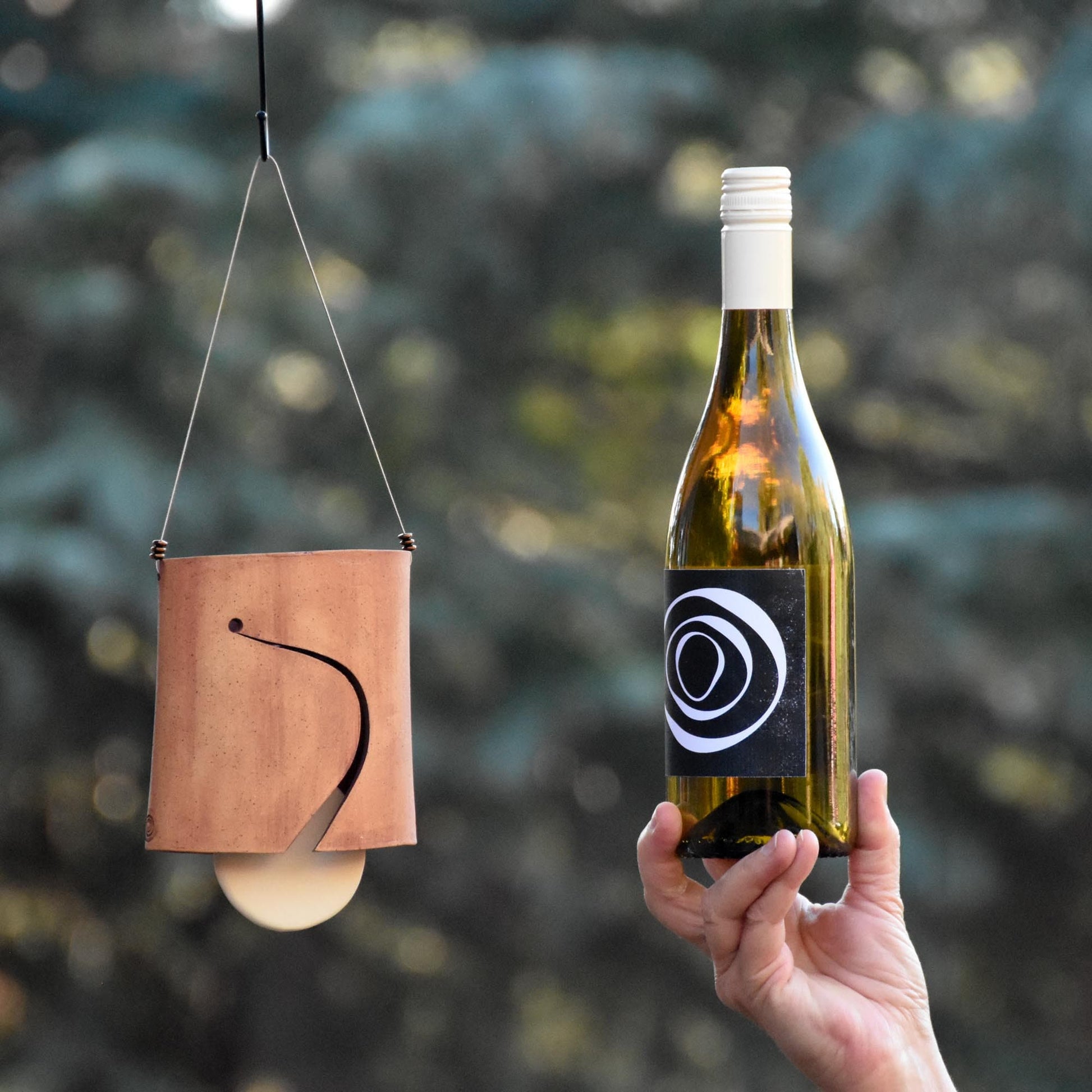Image showing speckled buff ceramic wind chime bell with white clapper and wine bottle next to it for size comparison
