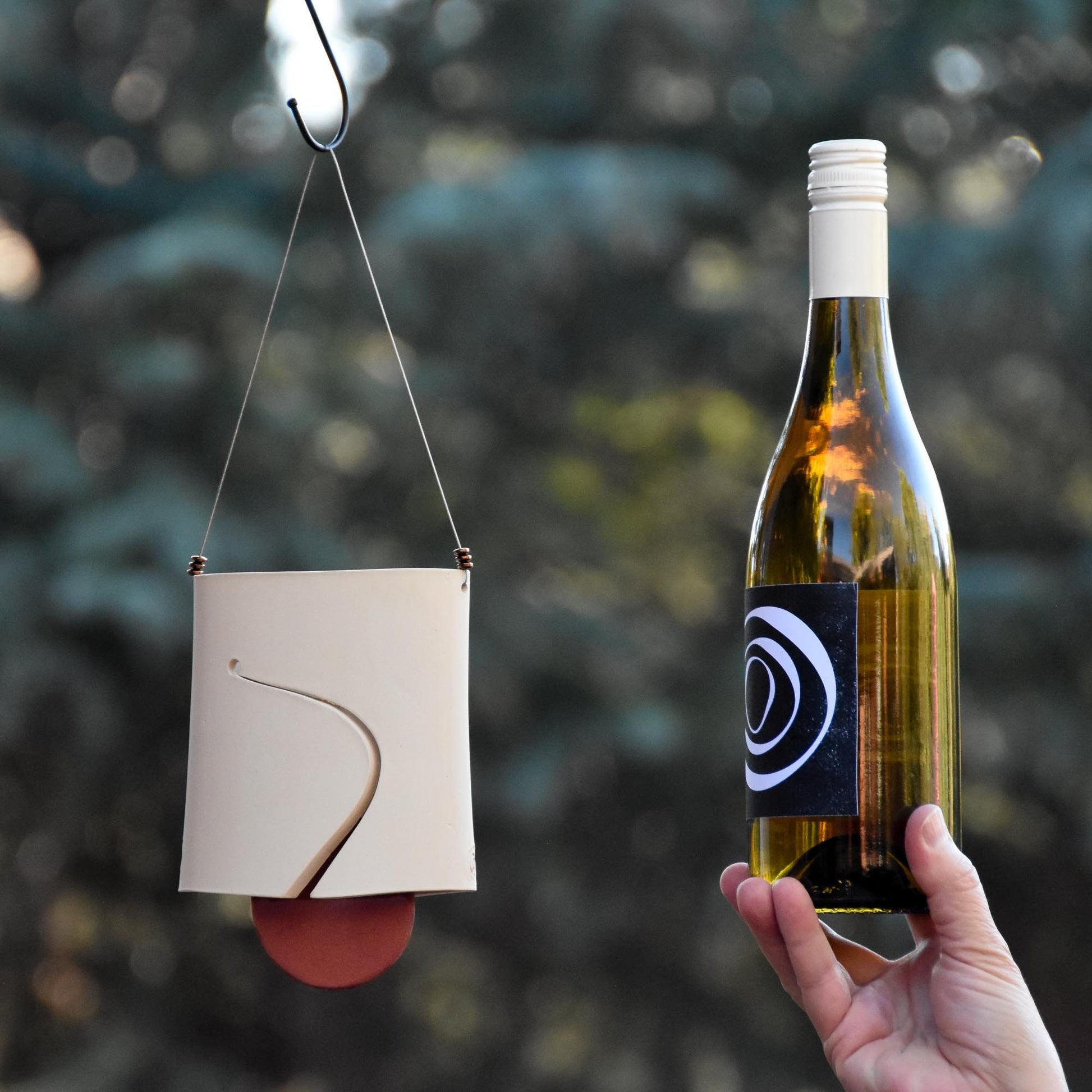 Image showing white ceramic wind chime bell with red clapper and wine bottle next to it for size comparison