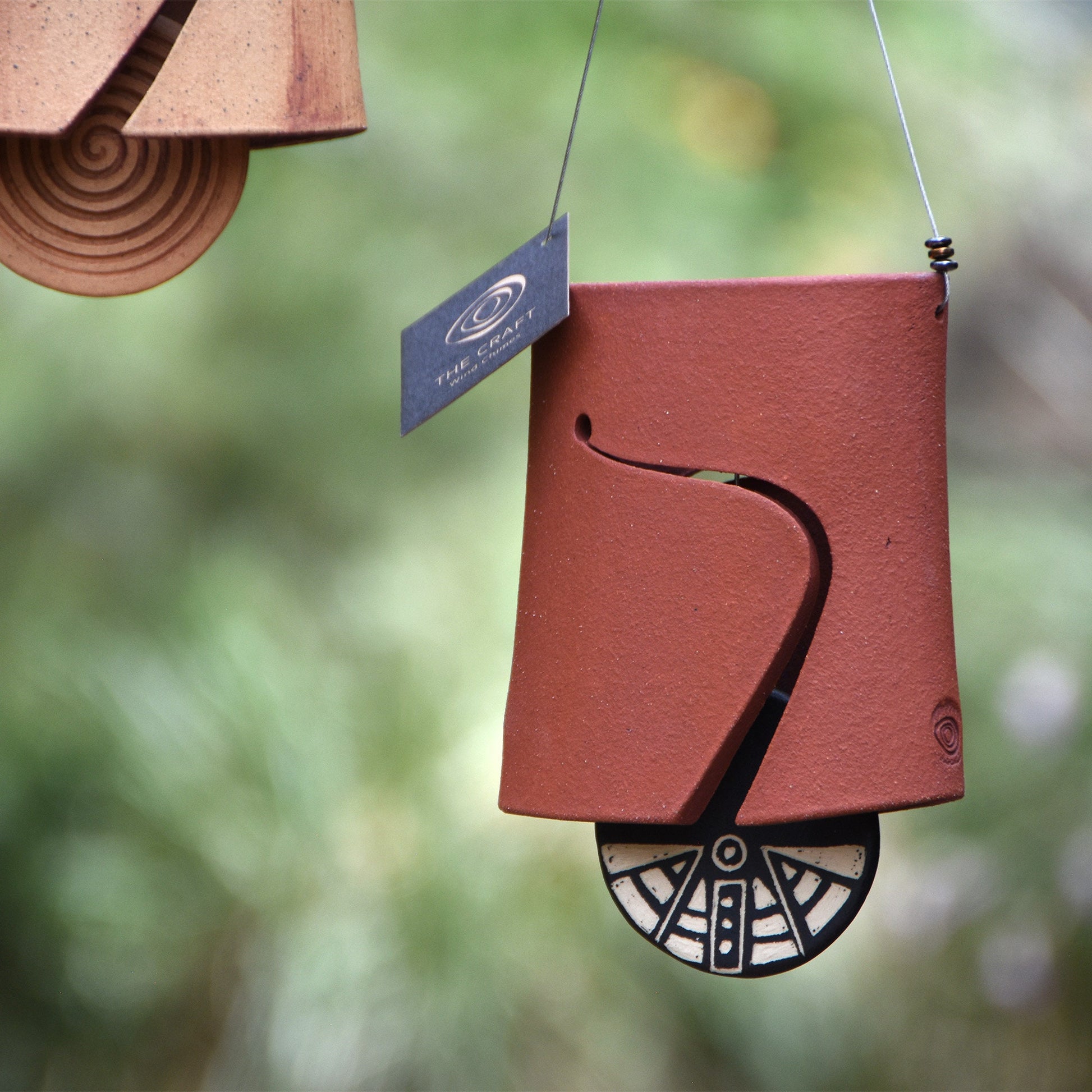 Closeup of modern, Hawaiian red wind chime bell showcasing a black and white wind clapper carved in an abstract style using the sgraffito technique