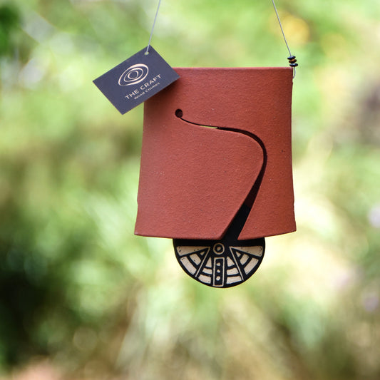 Closeup of modern, Hawaiian red wind chime bell showcasing a black and white wind clapper carved in an abstract motif using the sgraffito technique