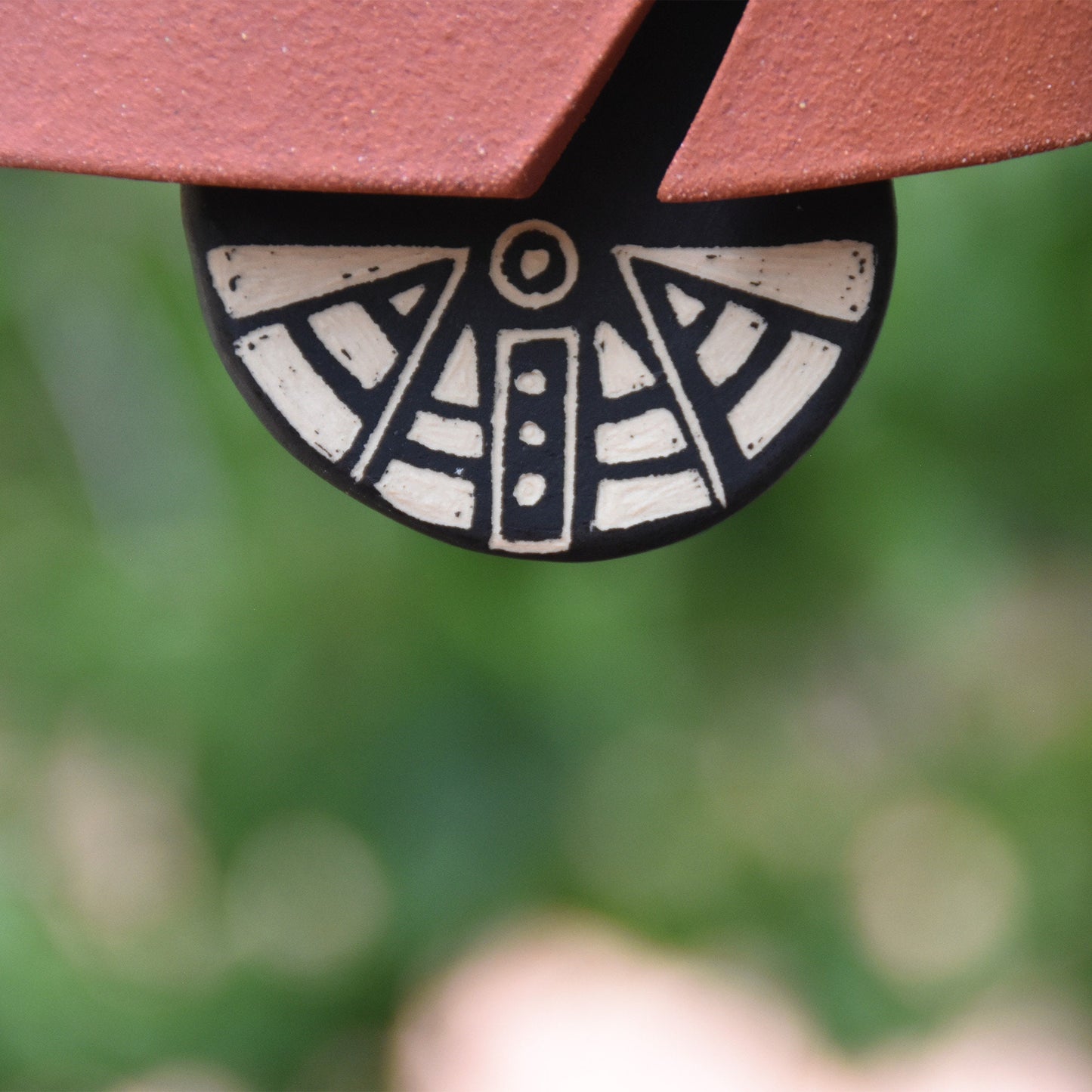 Closeup of modern black and white sgraffito wind clapper hanging from a rustic red colored wind chime