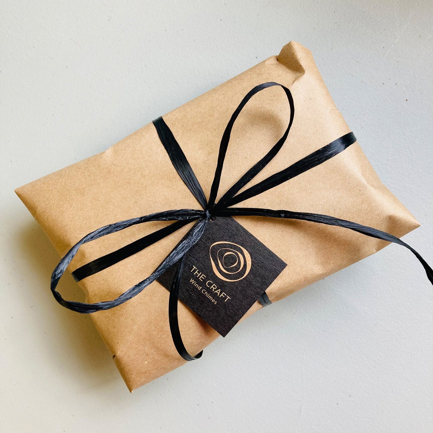 The Craft gift wrap image showing Kraft paper and black ribbon with The Craft Wind Chimes business card attached to it