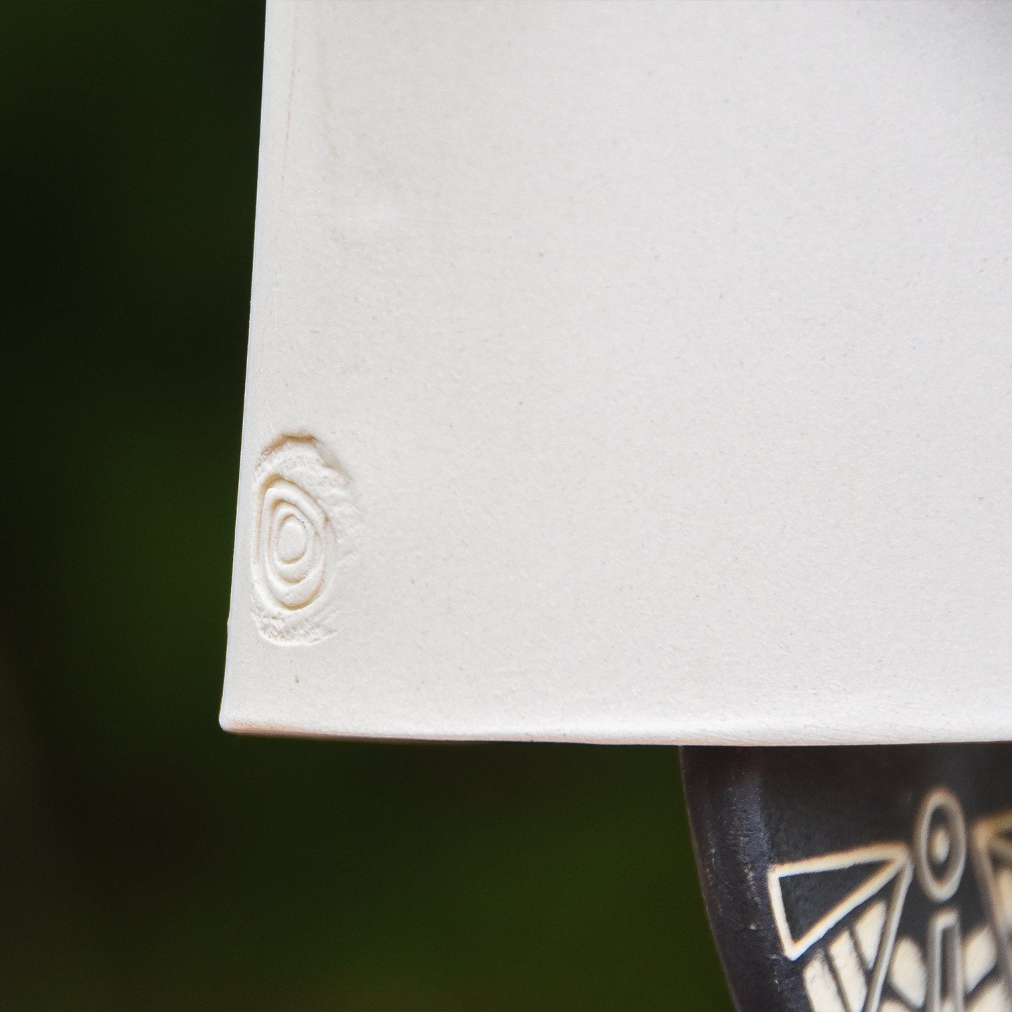 Closeup of the Craft logo stamped into a modern white wind chime bell featuring a black and white carved wind clapper with an abstract motif on both sides.