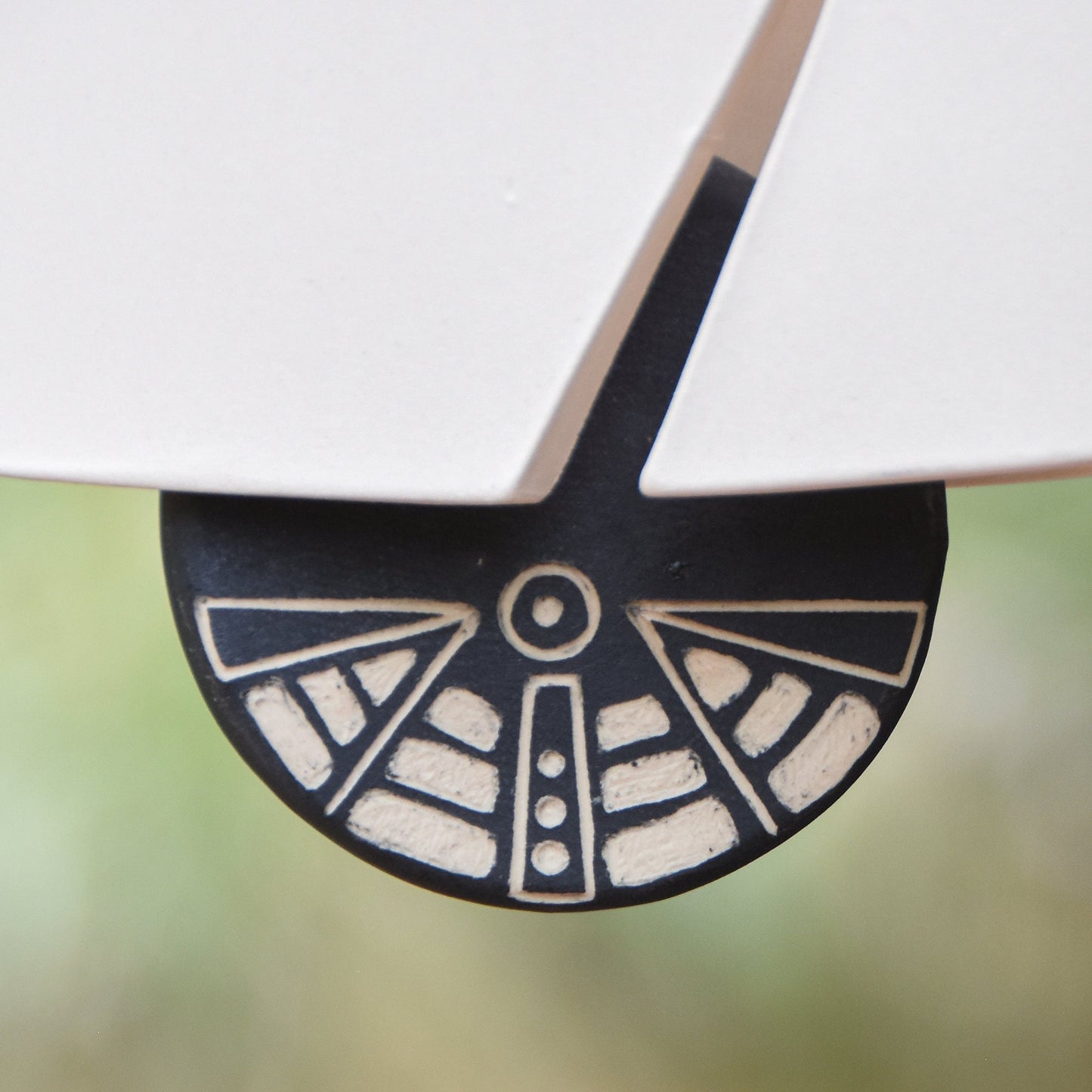 Closeup of black and white wind clapper carved with an abstract motif hanging from a white ceramic wind chime bell